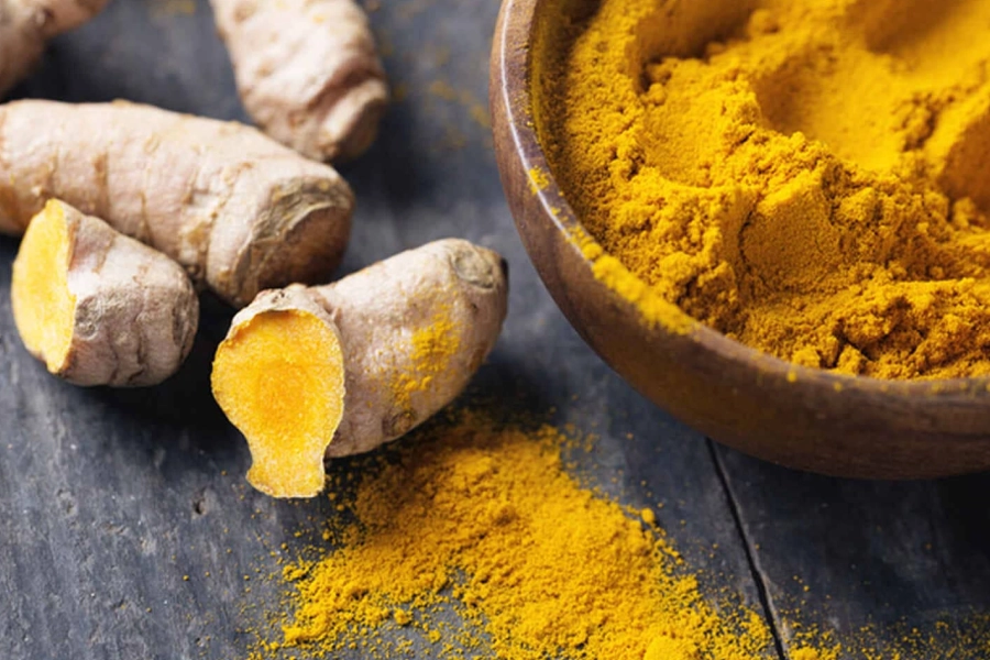 Raíz fresca y polvo de cúrcuma, representando el uso tradicional de la cúrcuma para el bienestar corporal.